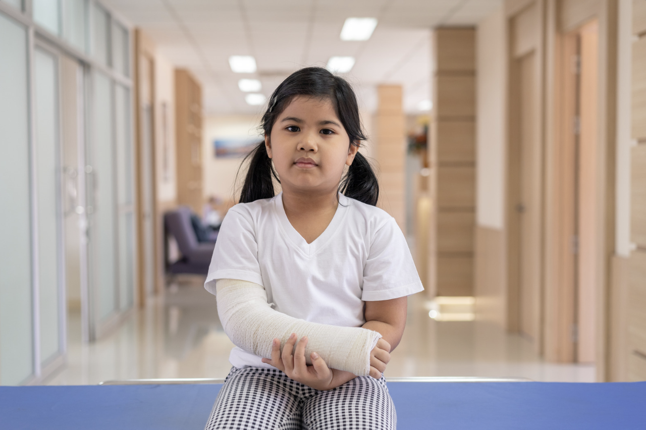 a little girl sitting at the end of the hospital with a broken arm