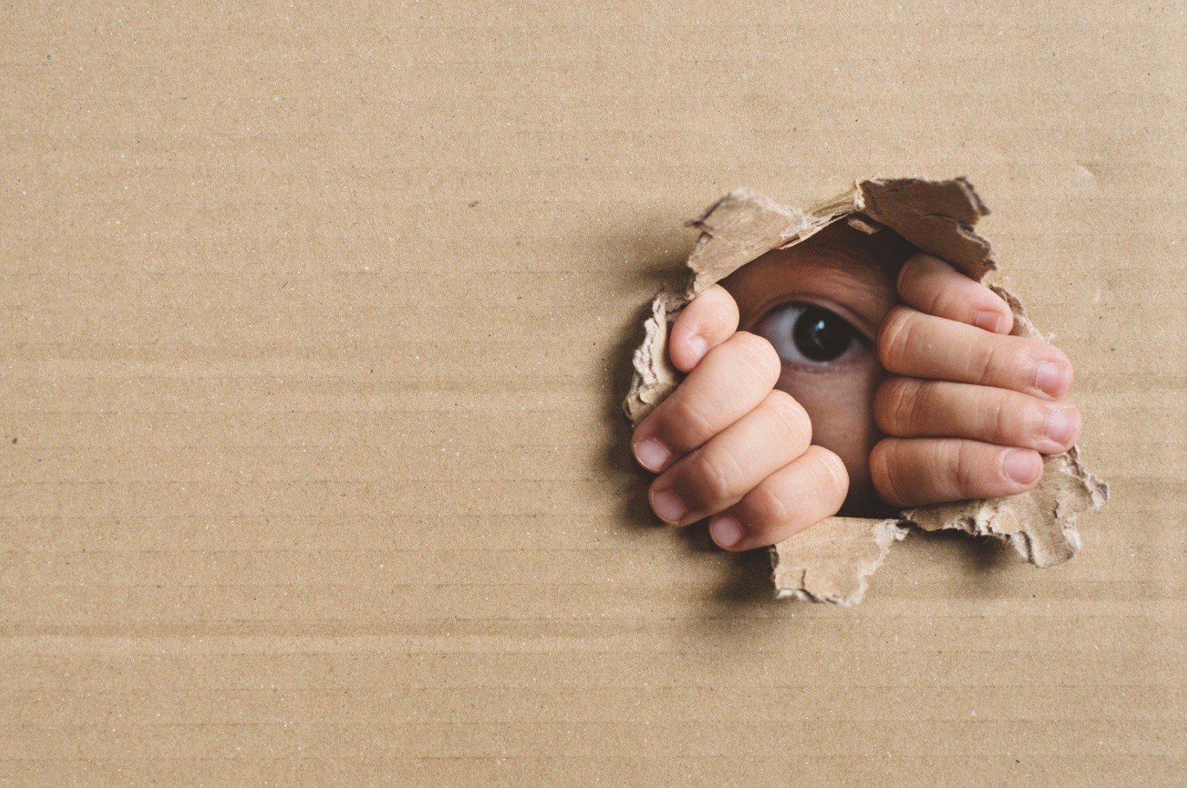 a girl peeping through a hole in a cardboard box 