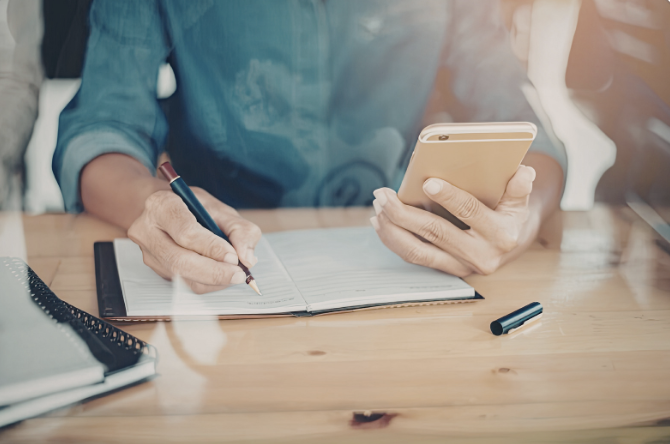 Person looking up information on a phone and writing notes.