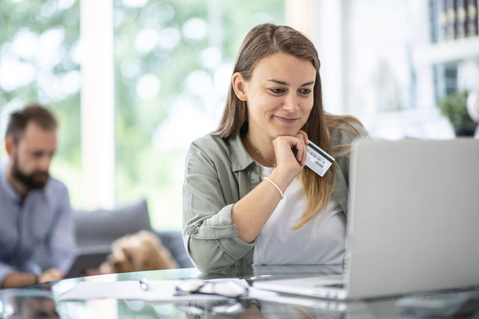 Woman holding a payment card while using a laptop at home 