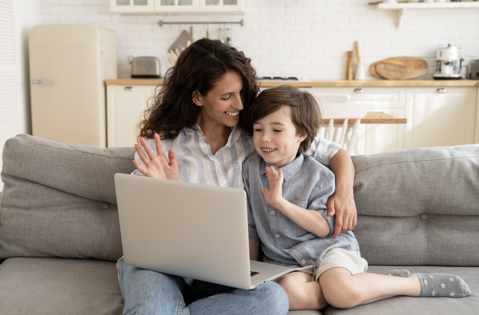 Mother and child waving during a video call on a laptop