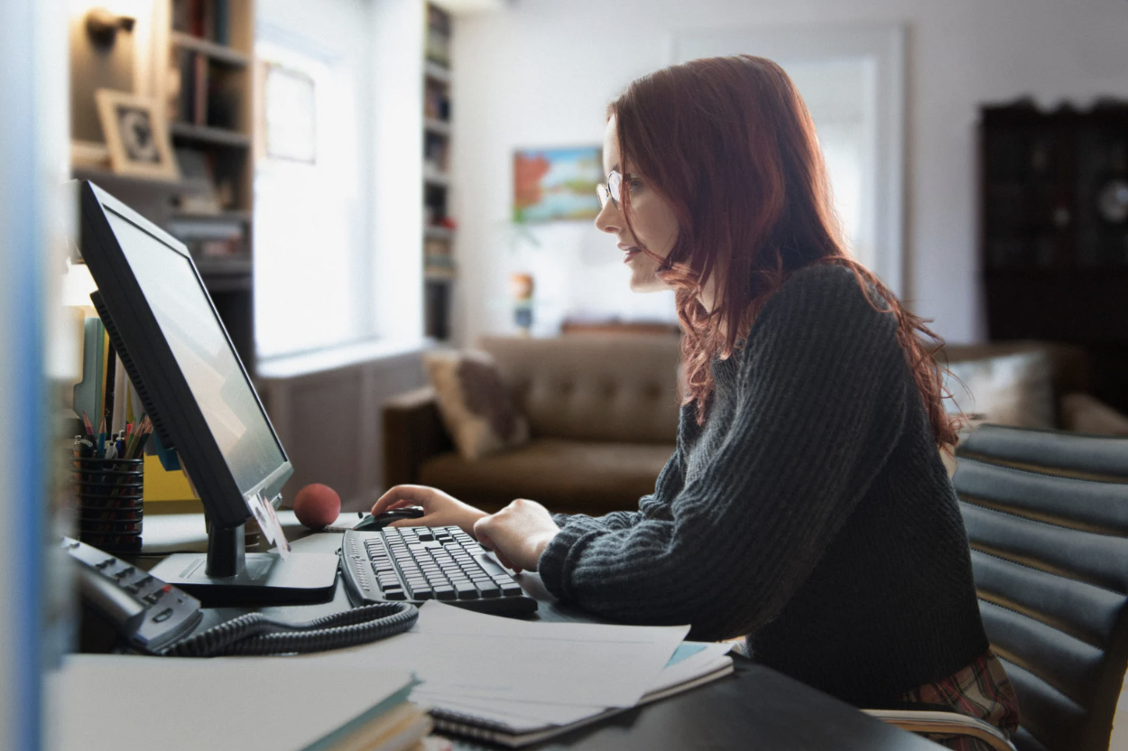 a woman doing computer work from home with files on the desk