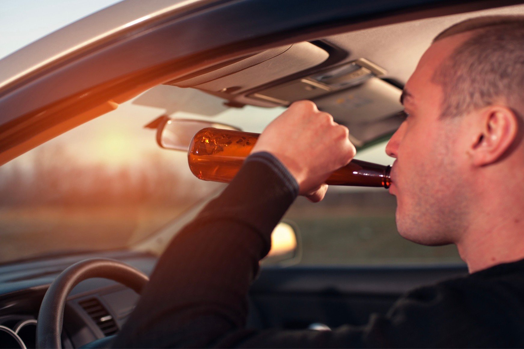 A man drinking a bottle of beer while driving