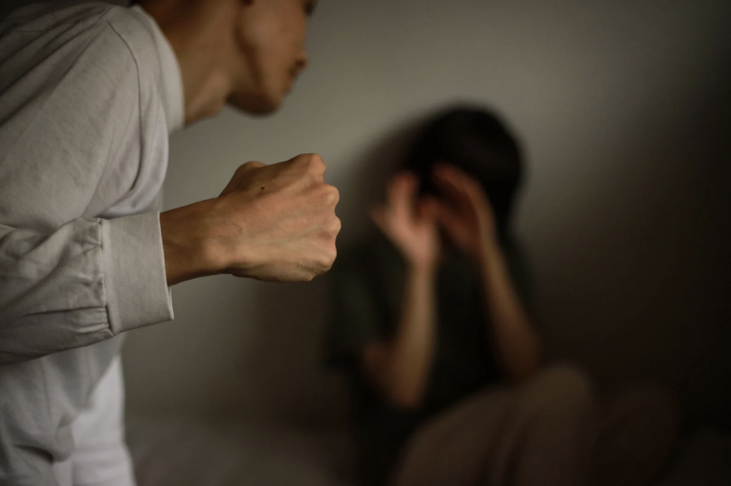 a person cowering and covering their face as another person approaches them with a fist