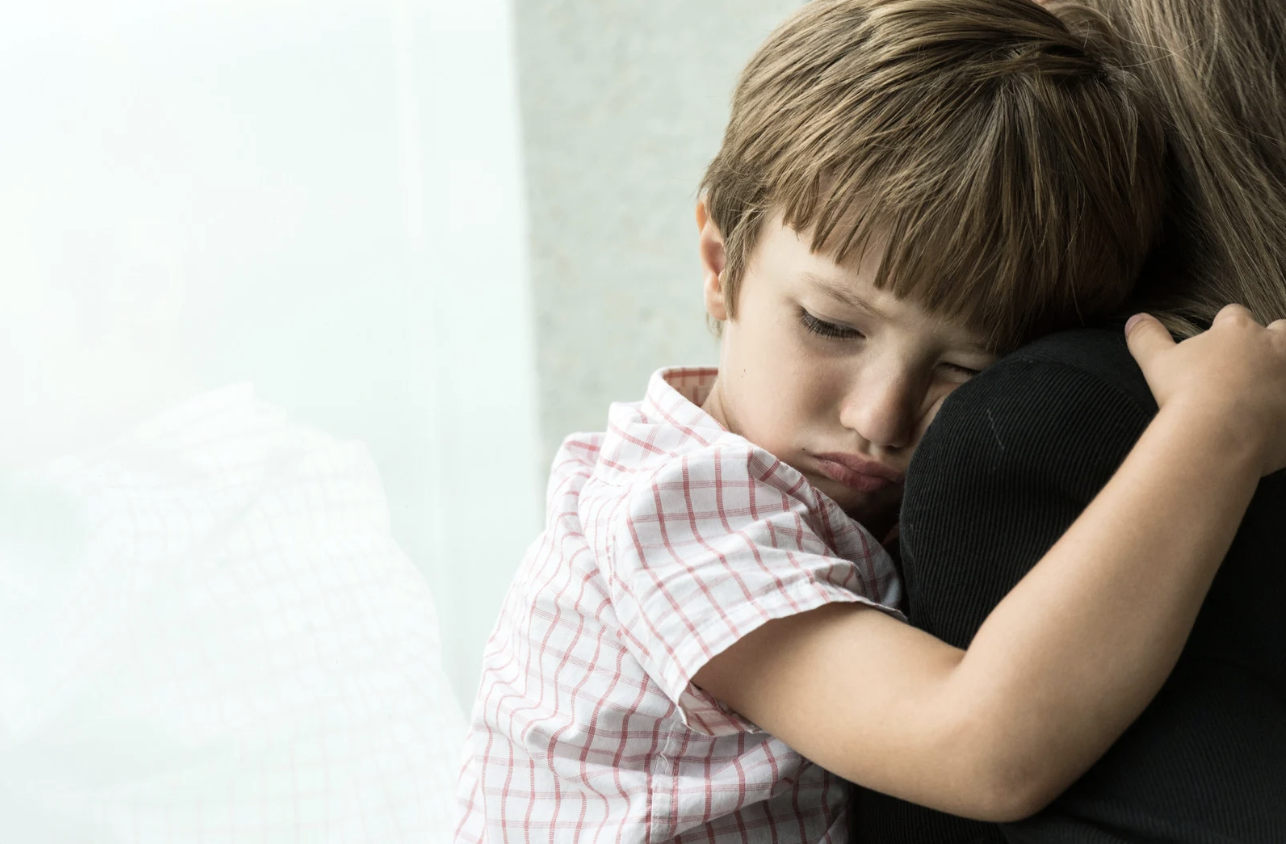 a sad child resting his head on an adults shoulder who is holding him up
