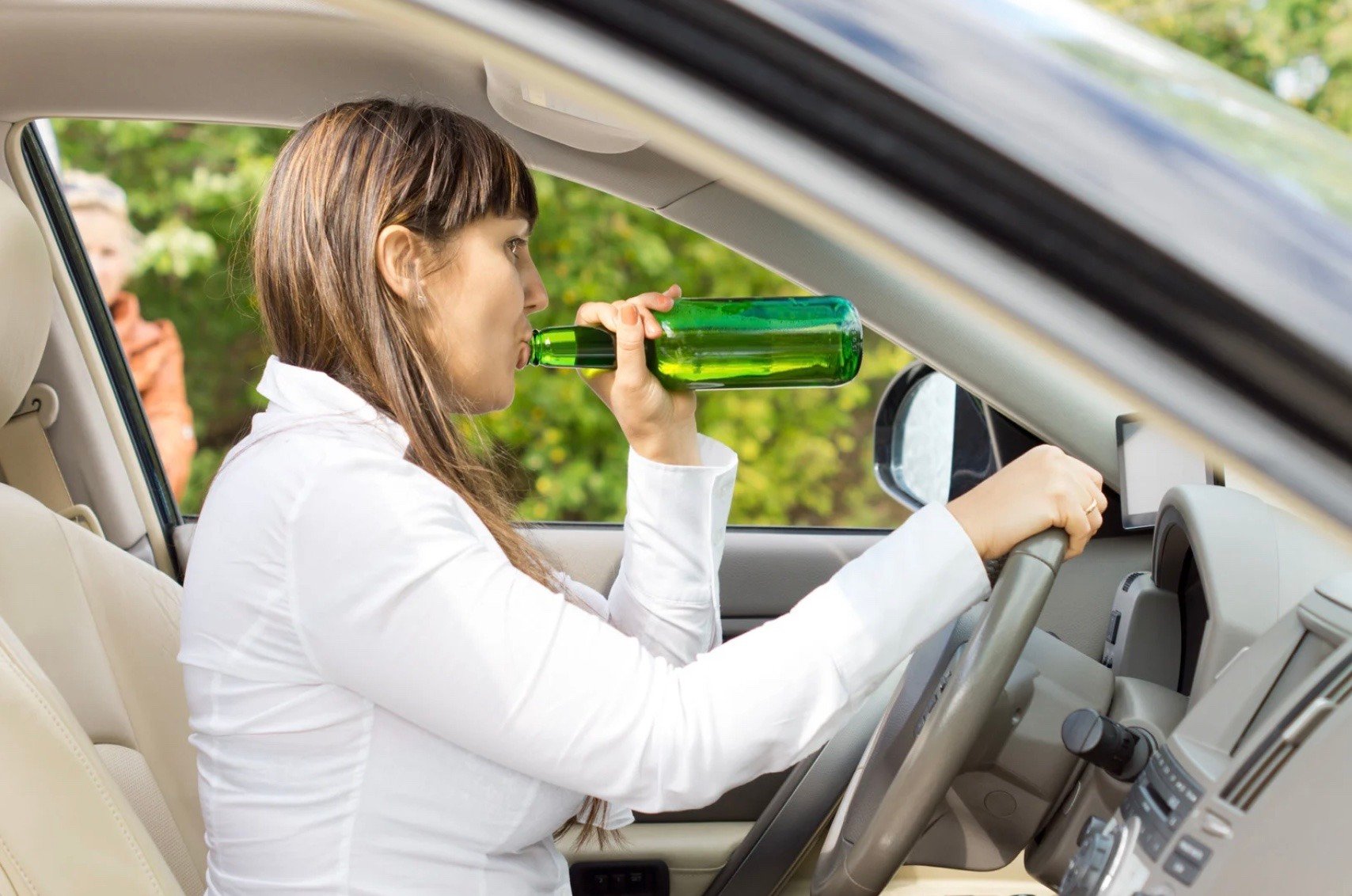 a woman drinking from an alcoholic bottle while driving 