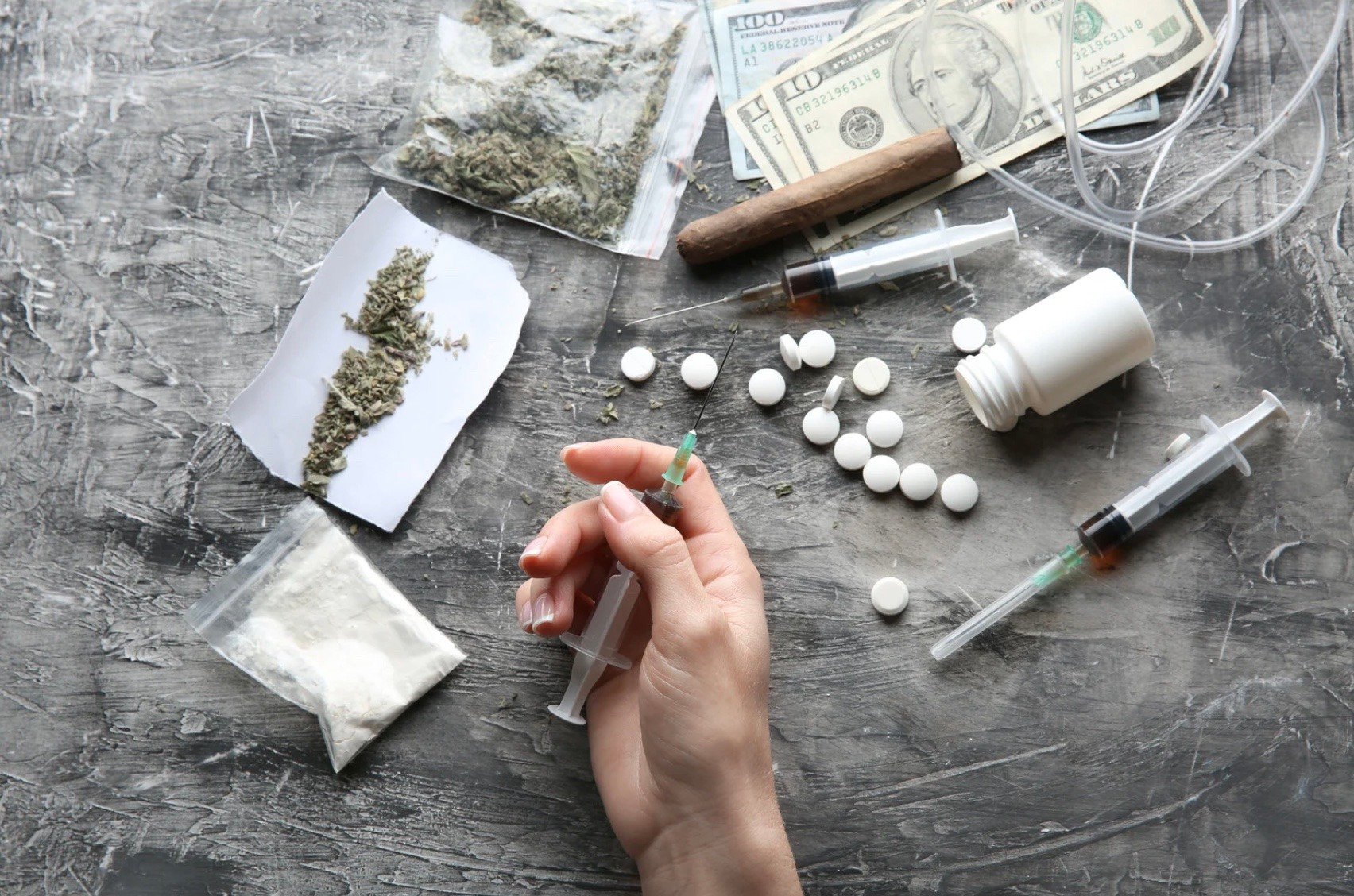 a person holding a syringe over a table with different drugs 