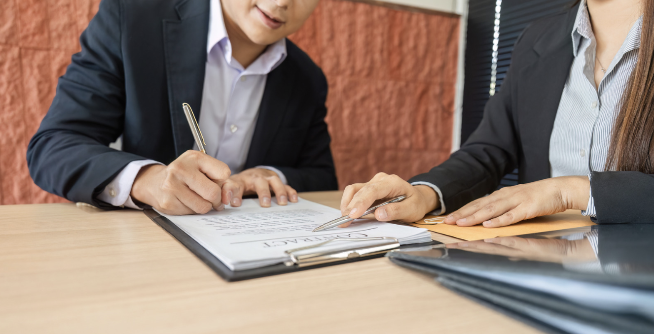 a man signing a contract at a table with a woman who gave him the contract