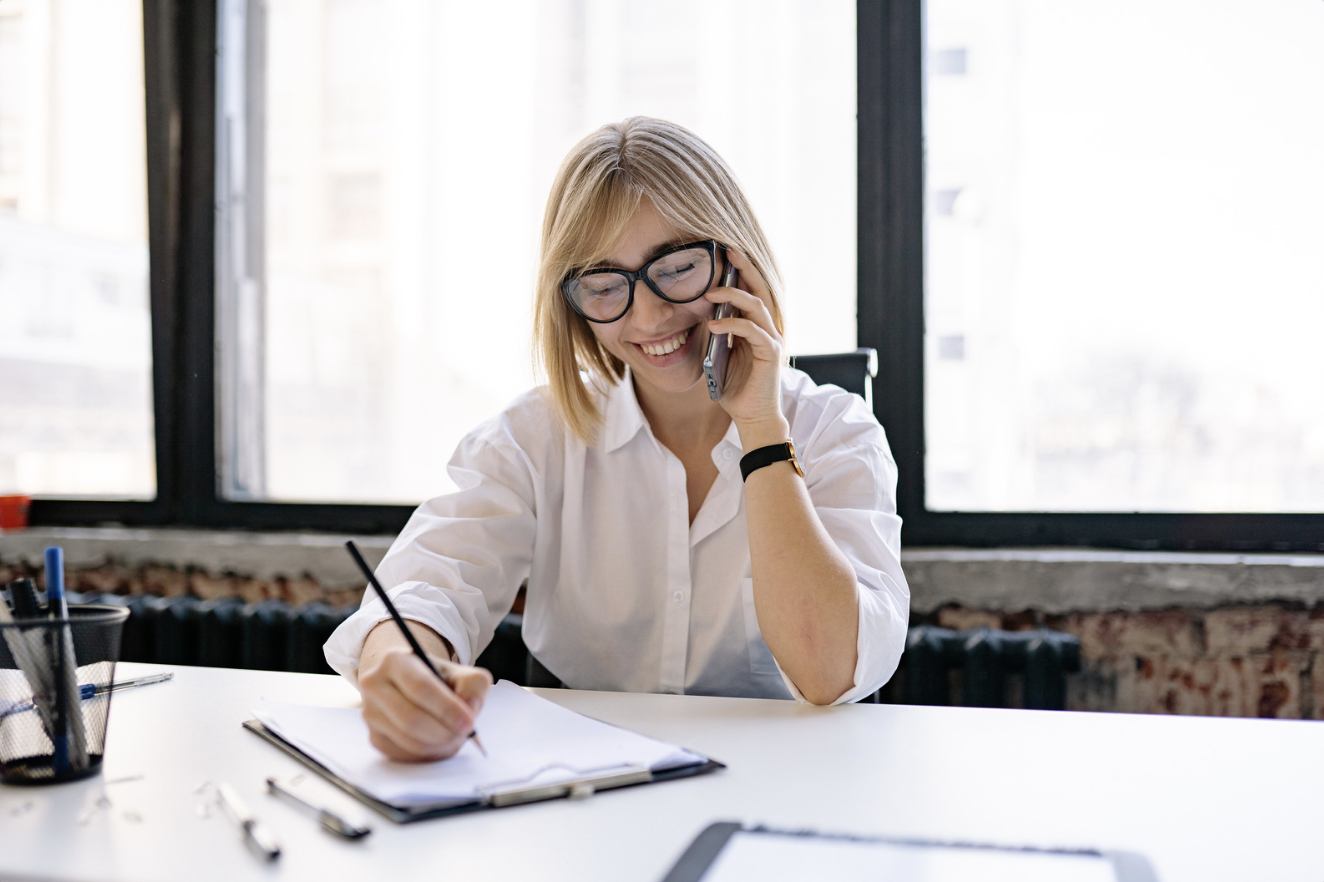 A woman taking notes while on a phone call