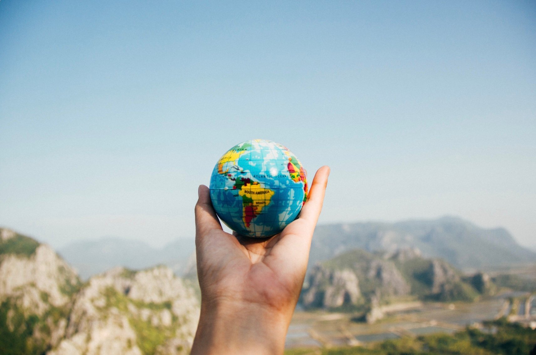 A hand holding a globe while standing outside