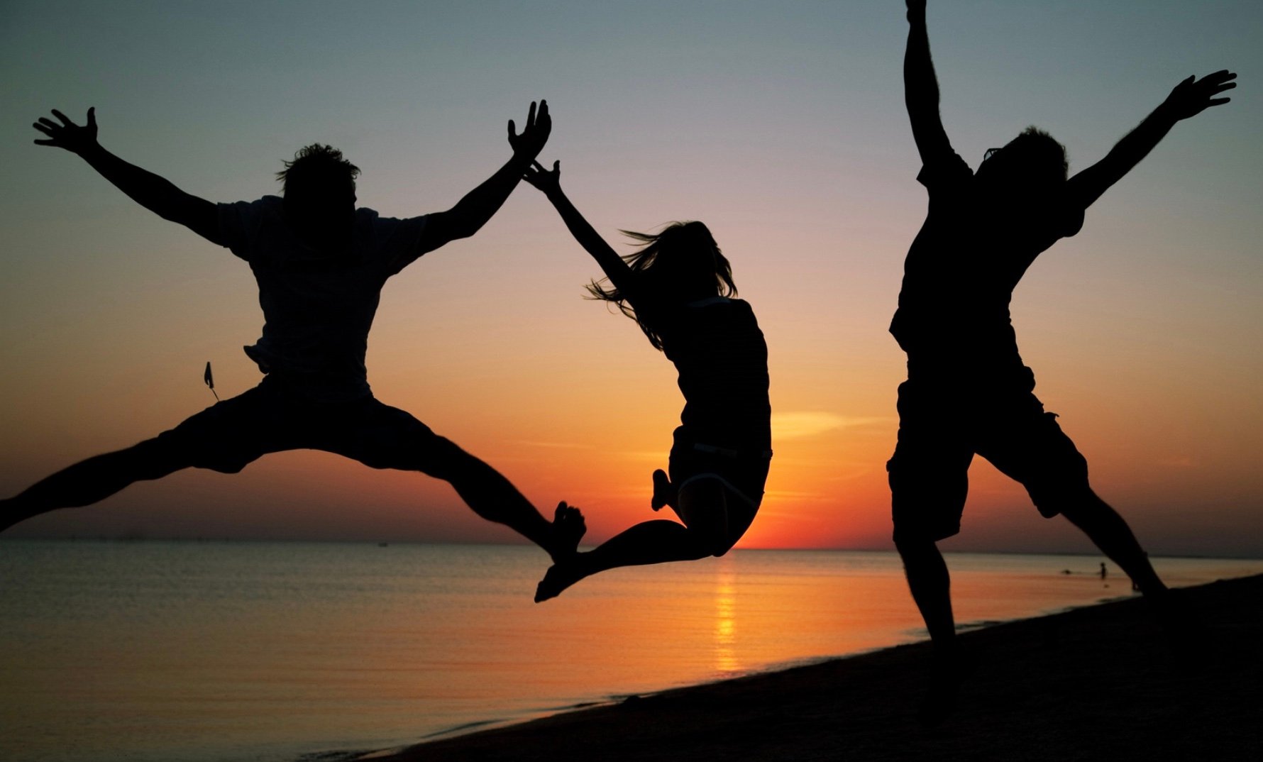 a group of people jumping into the air on a beach with a sunset