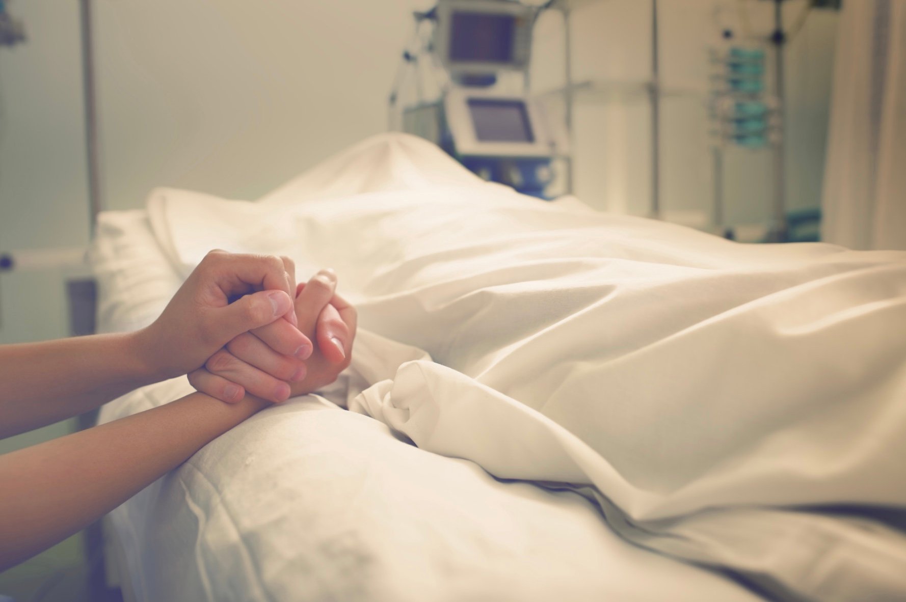 a person holding the hand of a loved one who has passed away in the hospital