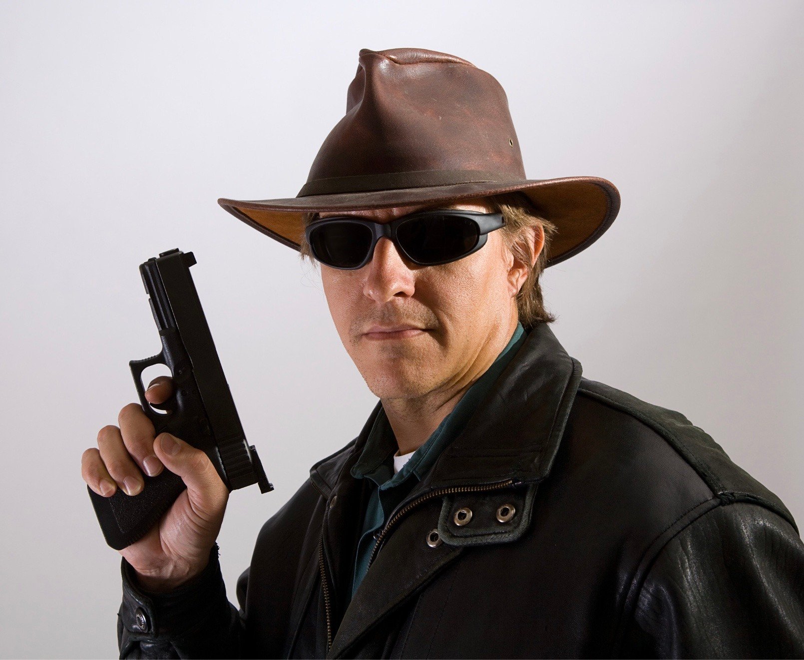 A bounty hunter holding a gun, pointed towards the ceiling while wearing a hat and sunglasses